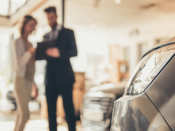 Blurred shot of dealership employee talking to customer in front of car.