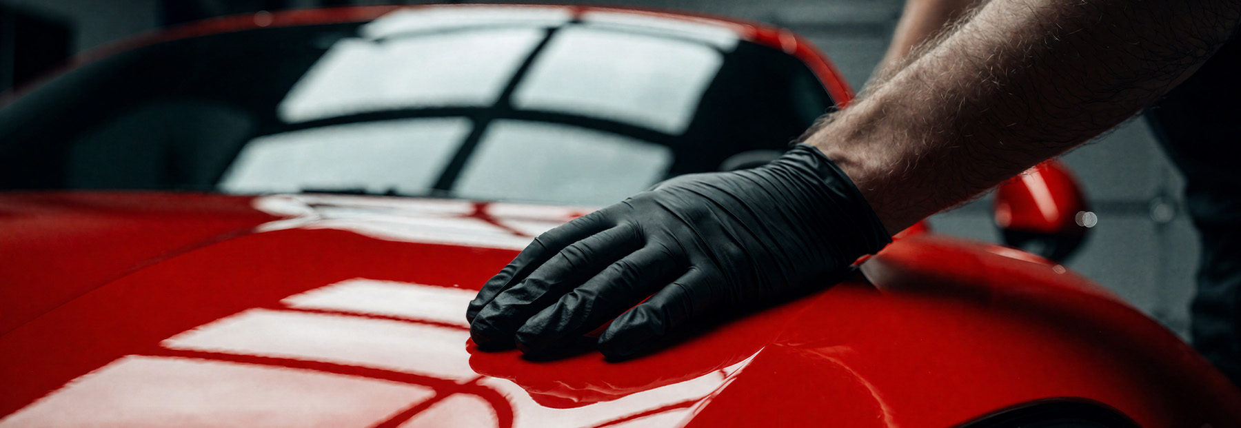 Professional Detailer Polishing Red Sports Car with Protective Gloves in Garage