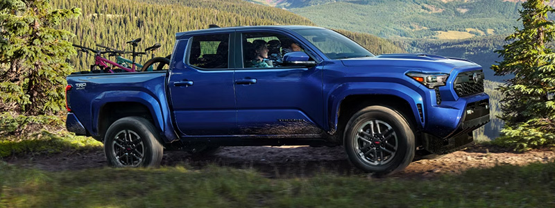 Side profile view of a blue Toyota Tacoma driving up a grassy mountain